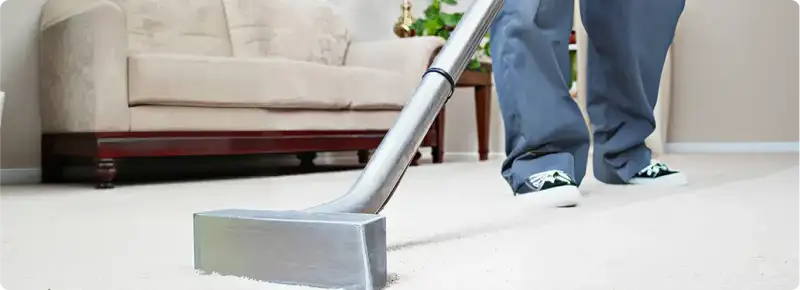 Carpet cleaning technician using a hot-water extraction wand on a light-colored carpet in a living room, Peoria, IL.