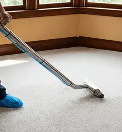Steam carpet cleaning technician using a hot-water extraction wand on a residential carpet, wearing blue protective shoe covers Peoria, IL.