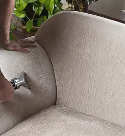 Professional upholstery cleaner deep-cleaning a fabric sofa with a handheld extraction tool and hose Peoria, IL.