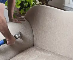 Professional upholstery cleaner deep-cleaning a fabric sofa with a handheld extraction tool and hose in Peoria, IL.